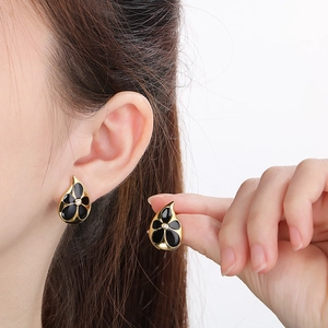 Detail of drop-shaped gold earrings with black flower pattern and zircon center