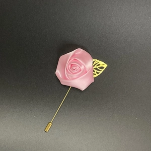 Detailed view of handmade pink silk rose boutonniere with golden leaf on dark surface