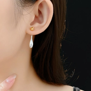 Close-up of dual-tone gold and silver teardrop earrings on a model with black background