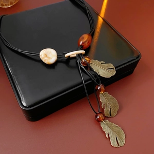 Detail of bohemian necklace with beige bead, metal feathers and amber charms on a box