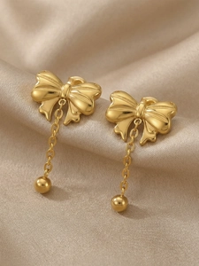 Detailed macro view of gold-plated bow earrings with tassel charms on beige silk fabric