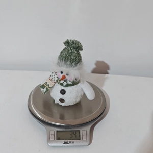 Digital scale showing the 34.1g weight of a Christmas snowman doll with a green knit hat