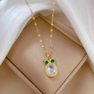 Golden owl necklace with green eyes and crystal pendant displayed in a jewelry box