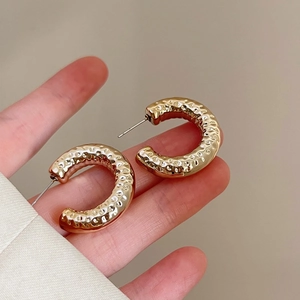 Detail of vintage golden C-shaped earrings with hammered metal texture for women