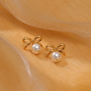 Macro shot of gold bow-shaped titanium earrings with elegant white pearls on champagne silk