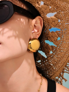 Close-up of polished 18k gold plated round disc earring worn by a model in a summer setting