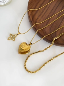 Détail de colliers en acier titane doré avec médaillon cœur et pendentif fleur en strass