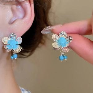 Detail of silver flower earrings with hammered texture and blue beaded tassel fringe