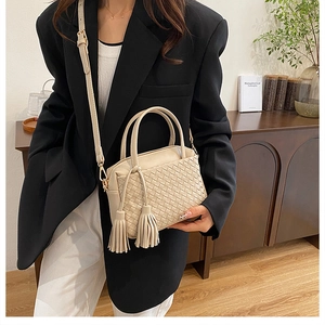 Detail of woven beige handbag with fringe tassel charms and elegant shoulder strap