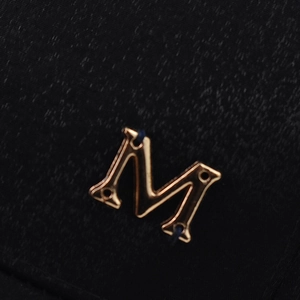 Détail macro de l'emblème métallique M doré poli sur un tissu noir texturé