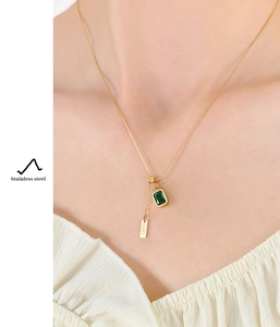 Detail of emerald zircon pendant and engraved BABY tag on a golden stainless steel necklace