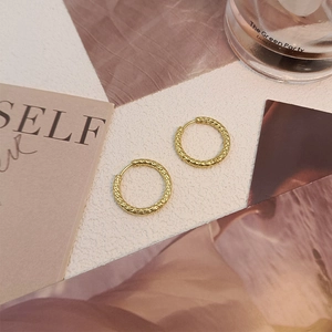 Detailed view of gold titanium steel hoop earrings with a textured hammered finish