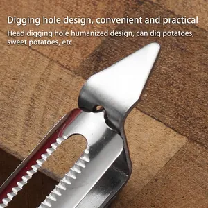 Stainless steel vegetable peeler with pointed tip for potato eye removal on wood
