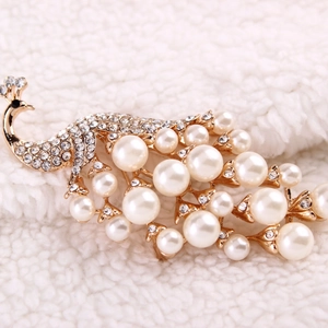 Elegant golden peacock brooch with faux pearls and rhinestones on soft white fabric