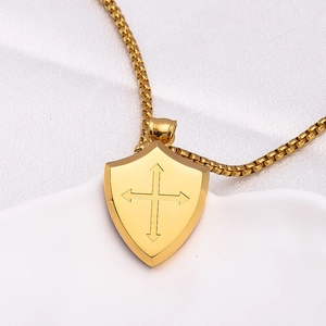 Polished gold stainless steel shield cross necklace displayed on white ceramic plate