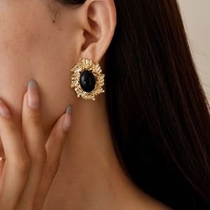 Close-up of vintage gold leaf earrings with black oval stones on a model's ear