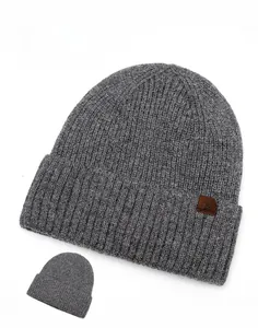 Detail of dark grey ribbed knit beanie with brown leather snowflake patch on white background