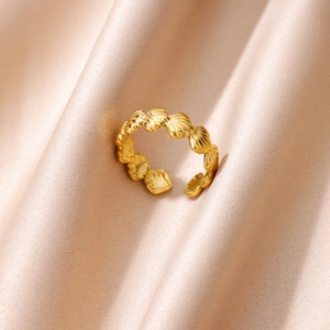 Detailed macro view of gold shell-shaped open ring on a luxury pink silk fabric