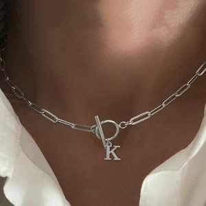 Detail of silver paperclip chain necklace featuring an OT buckle and letter K pendant
