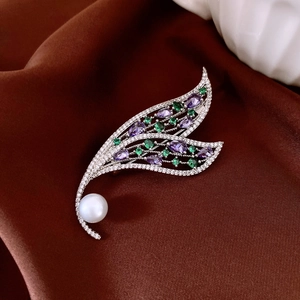 Macro shot of silver leaf brooch with purple gemstones, green jewels and white pearl