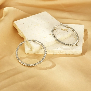 Close-up of silver twist hoop earrings with spiral rope texture on satin fabric
