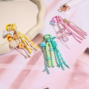Trois porte-clés perlés colorés avec breloques en résine et pompons sur fond rose