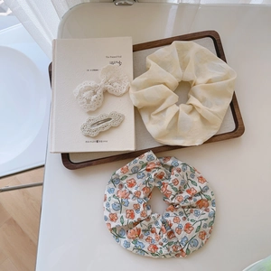 Detailed view of white lace bow clip and floral scrunchie set on a wooden tray
