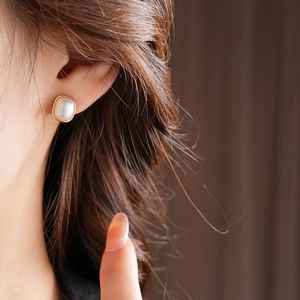 Close-up of elegant square pearl earrings with gold frames on a model's ear