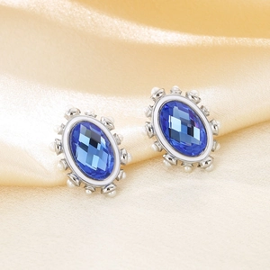 Detailed close-up of oval blue crystal earrings with pearl trim on silk background