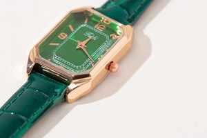 Macro detail of rectangle gold watch case with green leather strap and emerald dial
