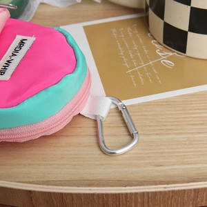 Mini round coin purse with pink and teal contrast design on a stylish wooden tray