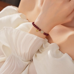 Detail of red bead bracelet with golden Fu charm and light stone on wrist