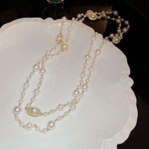 Elegant layered long pearl necklace with golden chains on white ceramic plate