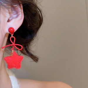Close-up of red velvet star earrings with bow and pearl detail worn by model
