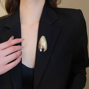 Close-up of a large gold teardrop brooch with mirror polish on a black suit blazer