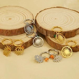 Detail of gold and silver evil eye hoop earrings with sunburst charms on wood surface