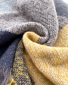Close-up of soft cashmere-like knit fabric with grey, blue, and yellow plaid texture