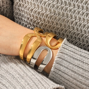 Detail of stacked gold and silver geometric open bangles on a grey knit sweater sleeve