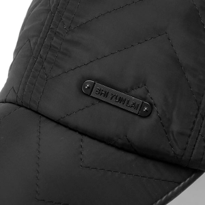 Macro shot of black quilted baseball cap fabric with a sleek matte metal nameplate detail