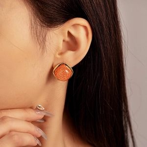 Close-up of a vintage resin earring with orange texture and a gold metal frame on an ear