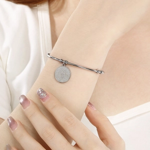 Detailed close-up of a silver stainless steel open bangle with engraved cross pendant