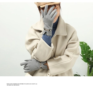 Detail of gray winter gloves featuring a black leather strap and golden horsebit buckle
