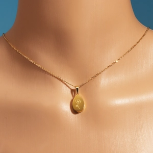 Détail d'un pendentif goutte d'eau doré avec gravure florale sur un collier fin