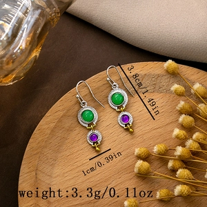Detail view of retro exotic earrings with green and purple stones on a wooden stand
