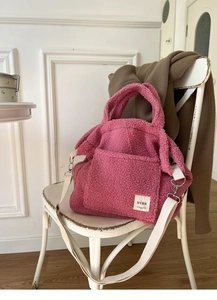 Detail of pink faux shearling tote with canvas strap and large front pocket on a chair