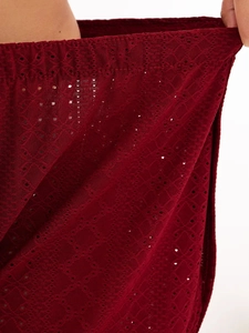 Macro detail of wine red eyelet fabric showing geometric镂空patterns and elastic waistband