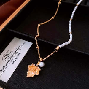 Dettaglio della collana con ciondolo a foglia d'acero in oro 18K e perle su scatola portagioie