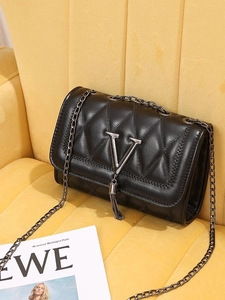 Chic black quilted leather crossbody bag with metal V-logo and tassel on velvet chair
