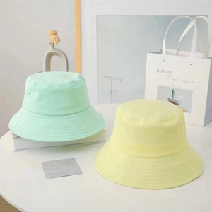 Minimalist cotton bucket hats in mint green and pale yellow shown on a white table