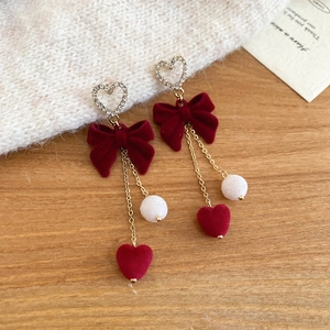 Detail of red velvet bow earrings with gold chains and sparkling crystals on wood